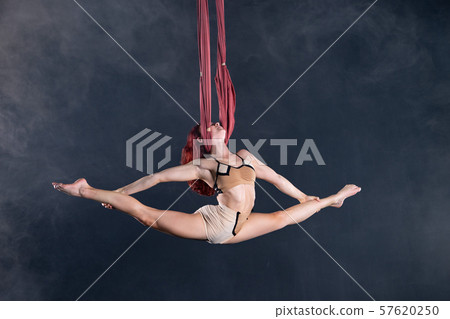Female athletic, sexy and flexible aerial circus artist with redhead dancing in the air on the silk Female athletic, sexy and flexible aerial circus artist with redhead dancing in the air on the silk 57620250