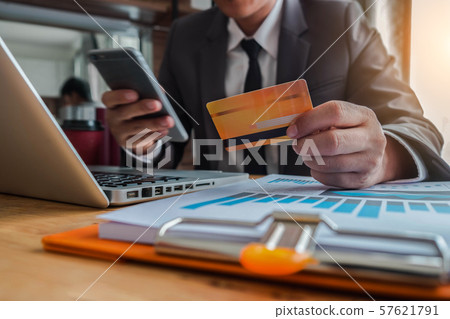 Male hold credit cards, conduct financial transactions via smartphone and data documents, put on the desk in the morning.  57621791