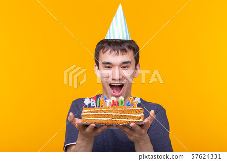 Portrait of a funny positive guy with a paper cap and glasses holding a congratulatory homemade cake 57624331