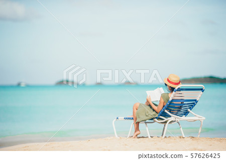 Young woman reading book on chaise-lounge on the beach 57626425
