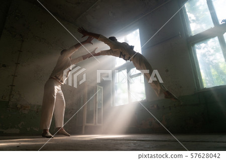 Male duo making acrobatic tricks wearing costume of insane people in abandoned room with sun rays 57628042