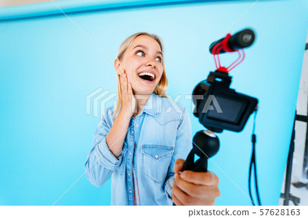 Beautiful girl blogger relieves itself at camera isolated blue background Beautiful girl blogger relieves itself at camera isolated blue background 57628163