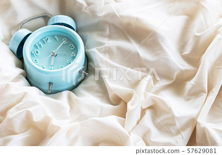 Blue classic alarm clock on white cream wrinkled bed sheet in the morning Blue classic alarm clock on white cream wrinkled bed sheet in the morning 57629081