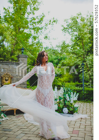 Seductive young bride in white negligee dancing with big piece of white fabric 57629352