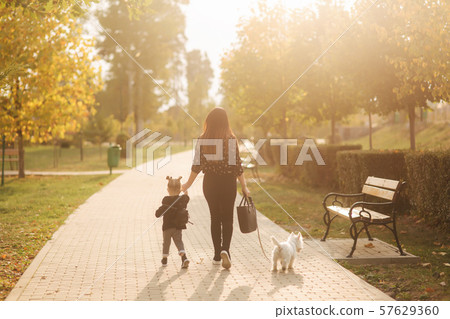 Woman and her daughter walk with his dog, autumn park. Happy family. Back view 57629360
