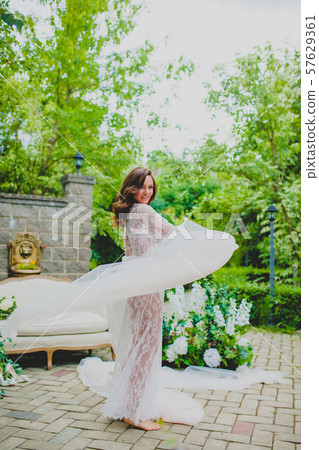 Seductive young bride in white negligee posing with big piece of white fabric 57629361