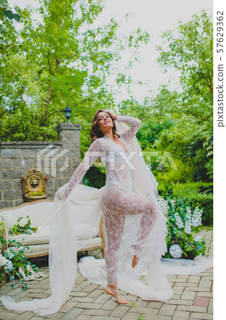 Seductive young bride in white negligee posing with big piece of white fabric Seductive young bride in white negligee posing with big piece of white fabric 57629362