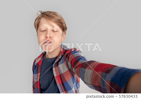 Freestyle. Young boy standing isolated on grey taking selfie tying to touch nose with tongue silly 57630433