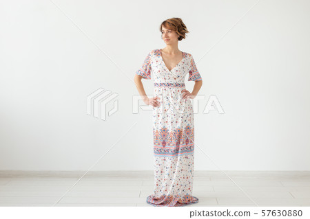 Charming young woman posing on a white background in a long light bright summer dress. The concept Charming young woman posing on a white background in a long light bright summer dress. The concept 57630880