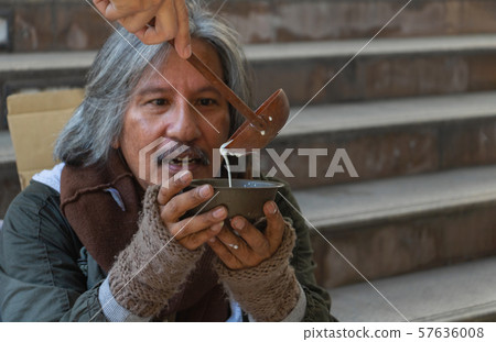 Homeless man is sitting down on walkway in town. He is receive milk. He is hoping to have the better life. poverty, despair, Photo Sympathetic and hope concept. Homeless man is sitting down on walkway in town. He is receive milk. He is hoping to have the better life. poverty, despair, Photo Sympathetic and hope concept. 57636008