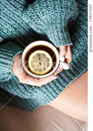 Female hands holding mug of hot tea with lemon in Female hands holding mug of hot tea with lemon in 57637507