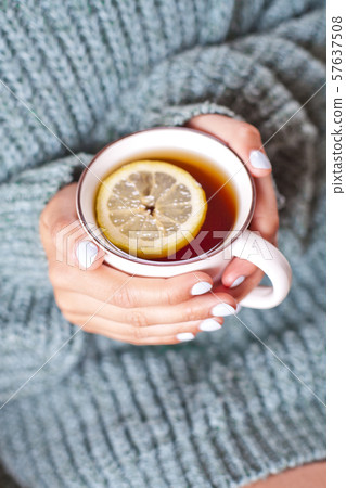Female hands holding mug of hot tea with lemon in Female hands holding mug of hot tea with lemon in 57637508