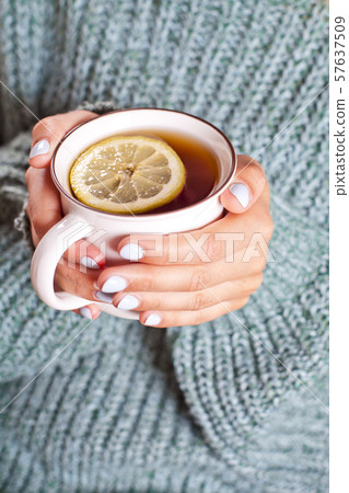 Female hands holding mug of hot tea with lemon in Female hands holding mug of hot tea with lemon in 57637509