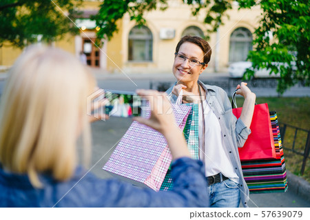 Beautiful brunette posing for smartphone camera holding shopping bags in street 57639079