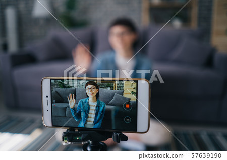 Joyful girl recording video with smartphone camera talking waving hand at home Joyful girl recording video with smartphone camera talking waving hand at home 57639190