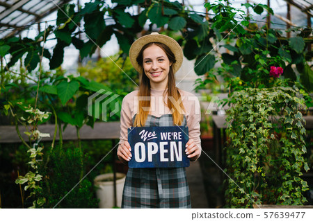 Beautiful lady standing in greenhouse with open sign smiling welcoming buyers 57639477