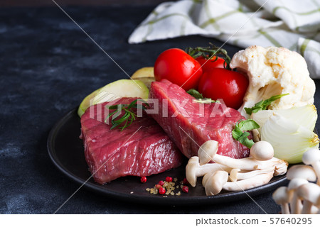 Raw beef steak on the bone with fresh vegetables in a grill pan on a concrete background, top view Raw beef steak on the bone with fresh vegetables in a grill pan on a concrete background, top view 57640295