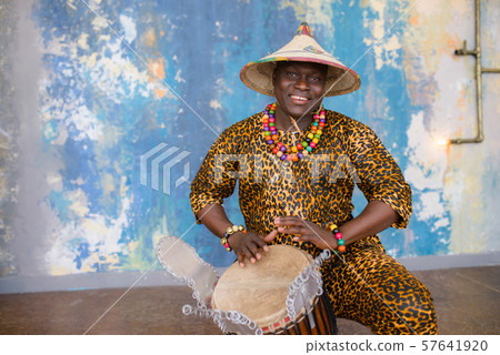Handsome african drummer weared in traditional costume playing on djembe drum 57641920