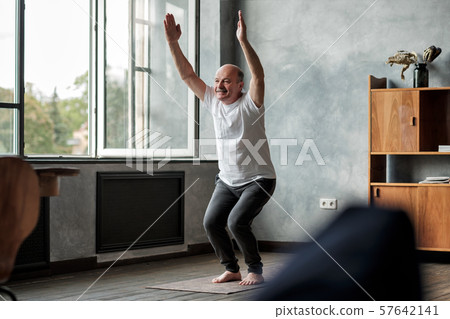 Man practicing yoga indoors at living room doing Chair pose or Utkatasana 57642141
