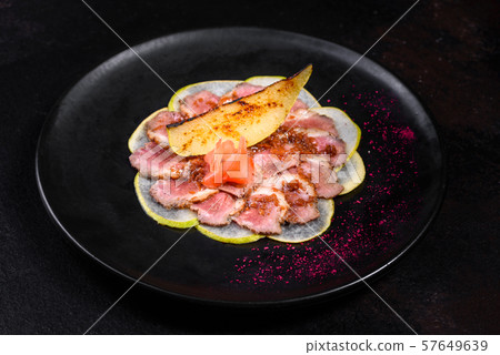 Edged pieces with caramelized pear on a black ceramic plate. Baked meat sliced with thin pieces 57649639