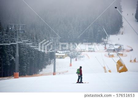 Back view of male skier standing on middle of slope and admiring foggy wooded mountains view Back view of male skier standing on middle of slope and admiring foggy wooded mountains view 57651653