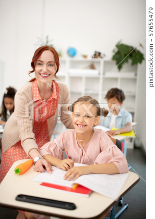 Cheerful schoolgirl smiling broadly while having interesting lesson Cheerful schoolgirl smiling broadly while having interesting lesson 57655479