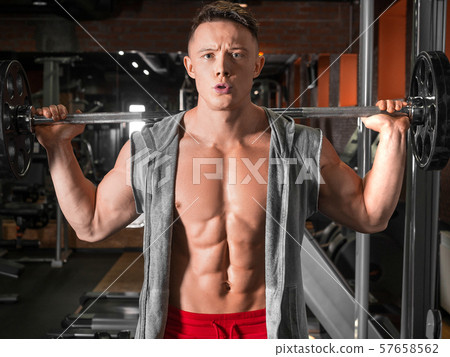 Front view of a young man man lifting a barbell in gym. Front view of a young man man lifting a barbell in gym. 57658562