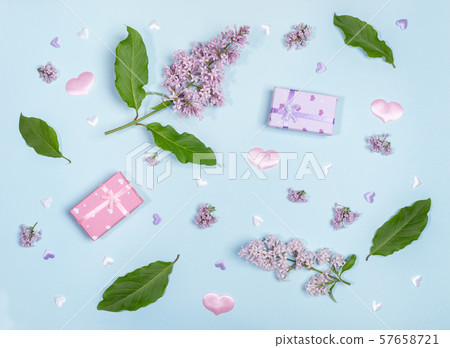 Composition with twigs, flowers and leaves of lilac, gift boxes and textile hearts on light blue background. Top view, flat lay. 57658721
