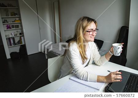 Young woman drinking coffee and working on laptop Young woman drinking coffee and working on laptop 57660872