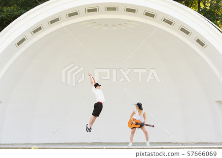 Woman playing guitar, man jumping next to her Woman playing guitar, man jumping next to her 57666069
