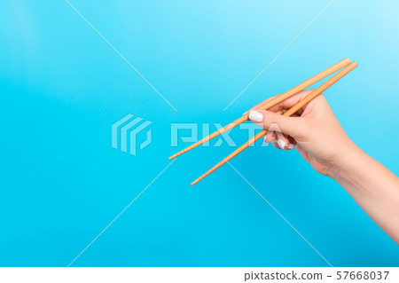 Female hand with chopsticks on blue background. Female hand with chopsticks on blue background. 57668037