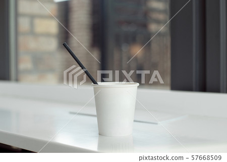 One simple takeaway paper cups on a white wooden table with a black paper tube. 57668509