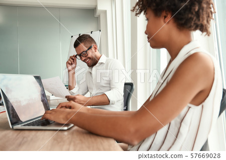 Working together. Young man in formal wear and eyeglasses looking at financial report and discussing Working together. Young man in formal wear and eyeglasses looking at financial report and discussing 57669028