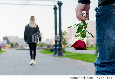 red rose flower in the hand of the guy on the background of the girl red rose flower in the hand of the guy on the background of the girl 57669134