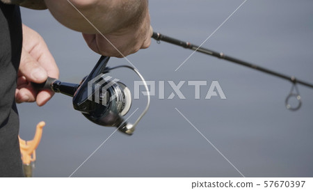 Male hand holding fishing rod and reeling the 57670397