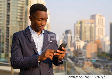 Young handsome African businessman using phone against view of the city 57672486
