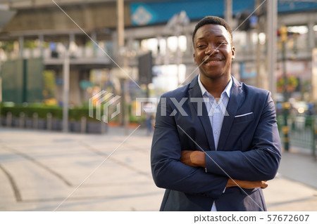 Young happy African businessman smiling with arms crossed in the city 57672607