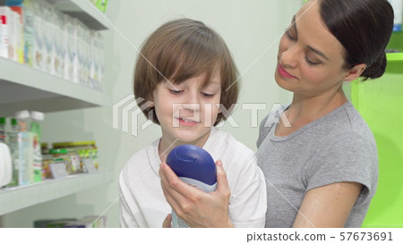 Beautiful woman choosing shower gel for her adorable son at drugstore Beautiful woman choosing shower gel for her adorable son at drugstore 57673691