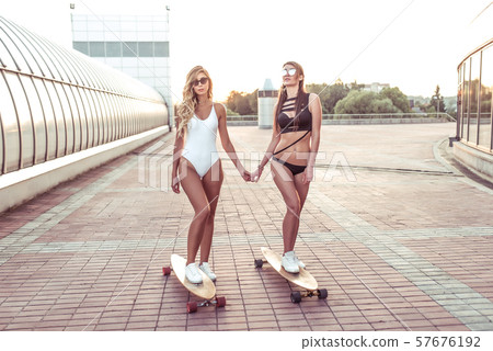 Two girls happy girlfriends ride hold hands skateboard, enjoy having fun playing, summer city Two girls happy girlfriends ride hold hands skateboard, enjoy having fun playing, summer city 57676192