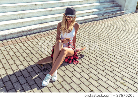 beautiful woman in summer in city sits, reads a message in a smartphone, watches video in phone 57676205