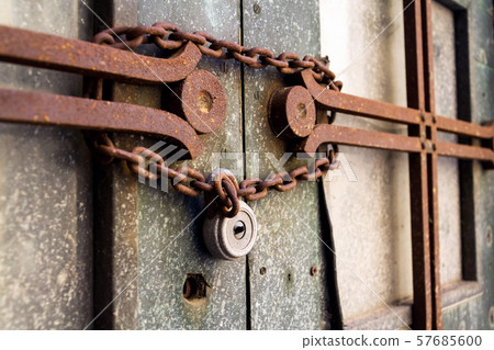 Old metallic padlock with rusty vintage chain hangs on old door, security concept 57685600