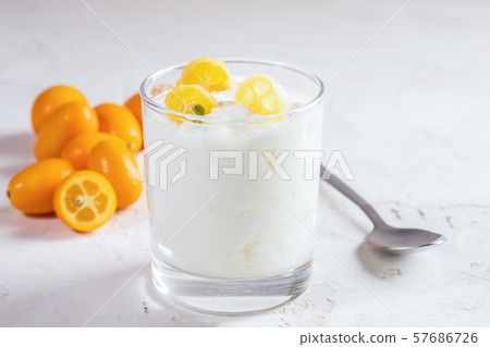 Close-up homemade yogurt with slices of exotic citrus fruit kumquat in transparent glass with whole fruits and metallic spoon on white background. 57686726