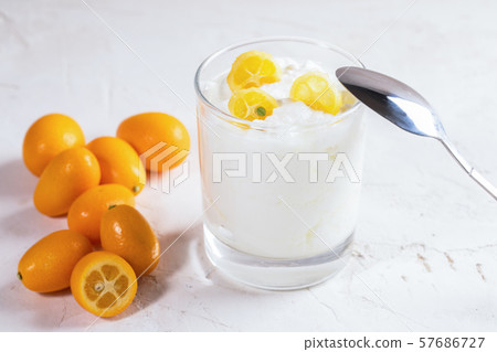 White homemade yogurt with slices of exotic citrus fruit kumquat in glass with metal spoon on it and  pile of whole fruits on white background. 57686727