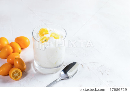 White homemade yogurt with slices of exotic citrus fruit kumquat in transparent glass, whole fruits and metallic spoon on white background with copy space. 57686729