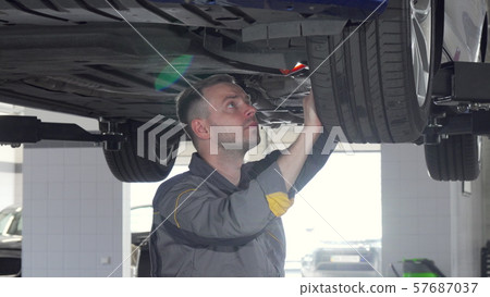 Sliding shot of auto mechanic checking SUV suspension of a lifted car 57687037