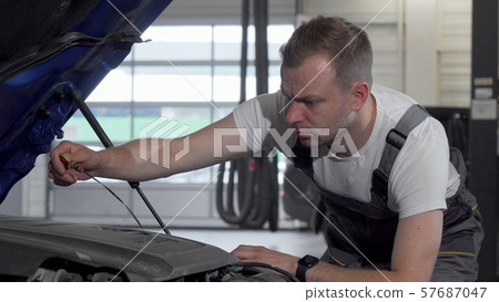 Mature auto mechanic checking oil in a car with open hood 57687047