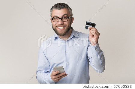 Cheerful man recommending credit card, holding cellphone Cheerful man recommending credit card, holding cellphone 57690528