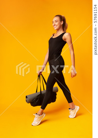 Smiling Lady Carrying Gym Bag With Rolling Mat, Yellow Background 57691154