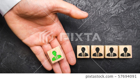 A hand holds out a green leader figure to a team of employees. Headhunter recruits staff and business personnel management. The concept of finding Specialists and workers on the job. A hand holds out a green leader figure to a team of employees. Headhunter recruits staff and business personnel management. The concept of finding Specialists and workers on the job. 57694091