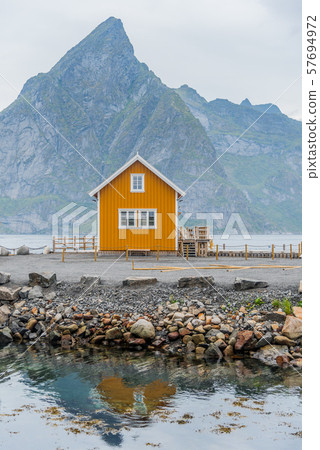 A yellow fishing cabin in Sakrisoy, a small fishing village in Moskenes Municipality on Lofoten islands in Nordland county, Norway with a mountain in background A yellow fishing cabin in Sakrisoy, a small fishing village in Moskenes Municipality on Lofoten islands in Nordland county, Norway with a mountain in background 57694972